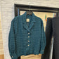 Blue textured sweater on a hanger against a white brick wall.