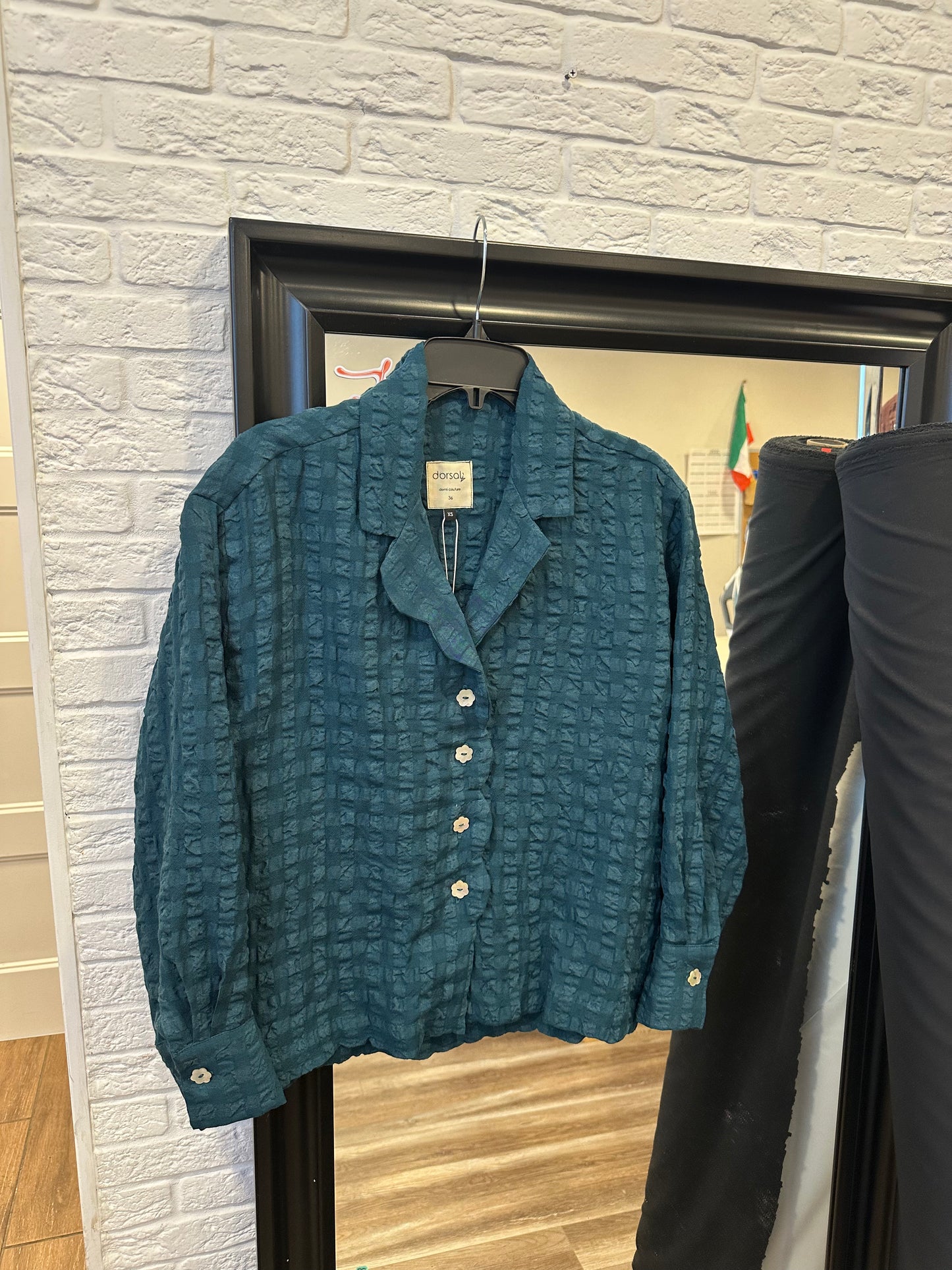 Blue textured sweater on a hanger against a white brick wall.
